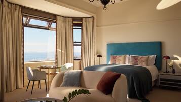 Habitación de hotel con cama, sofá, sillón, mesa y vista al océano.