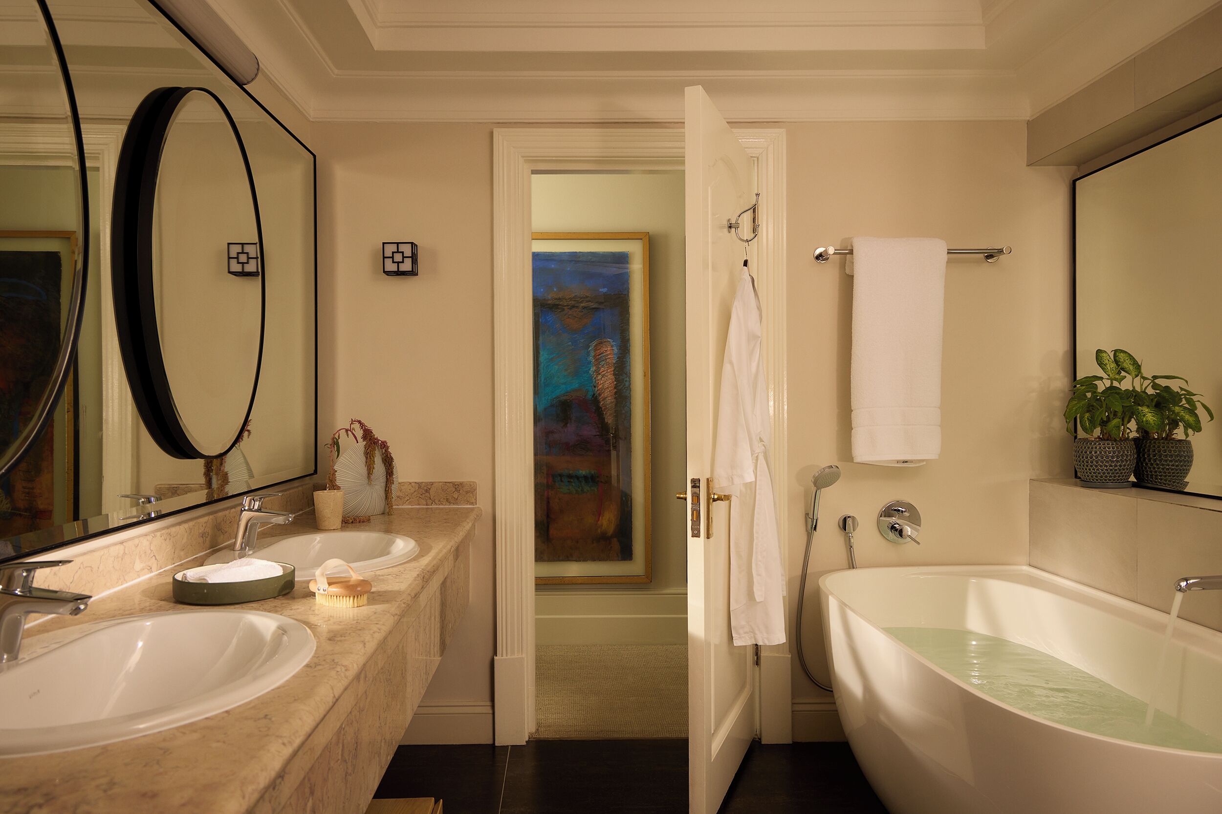 A bathroom with two sinks, a bathtub, a mirror, and a painting in the background.