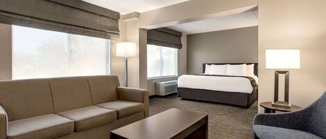 A hotel room with a sofa, a chair, a bed, a bedside table, and a lamp.