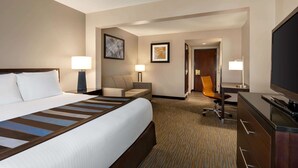 Een hotelkamer met een groot bed, een bureau, een stoel, een televisie en een deur naar een andere kamer.