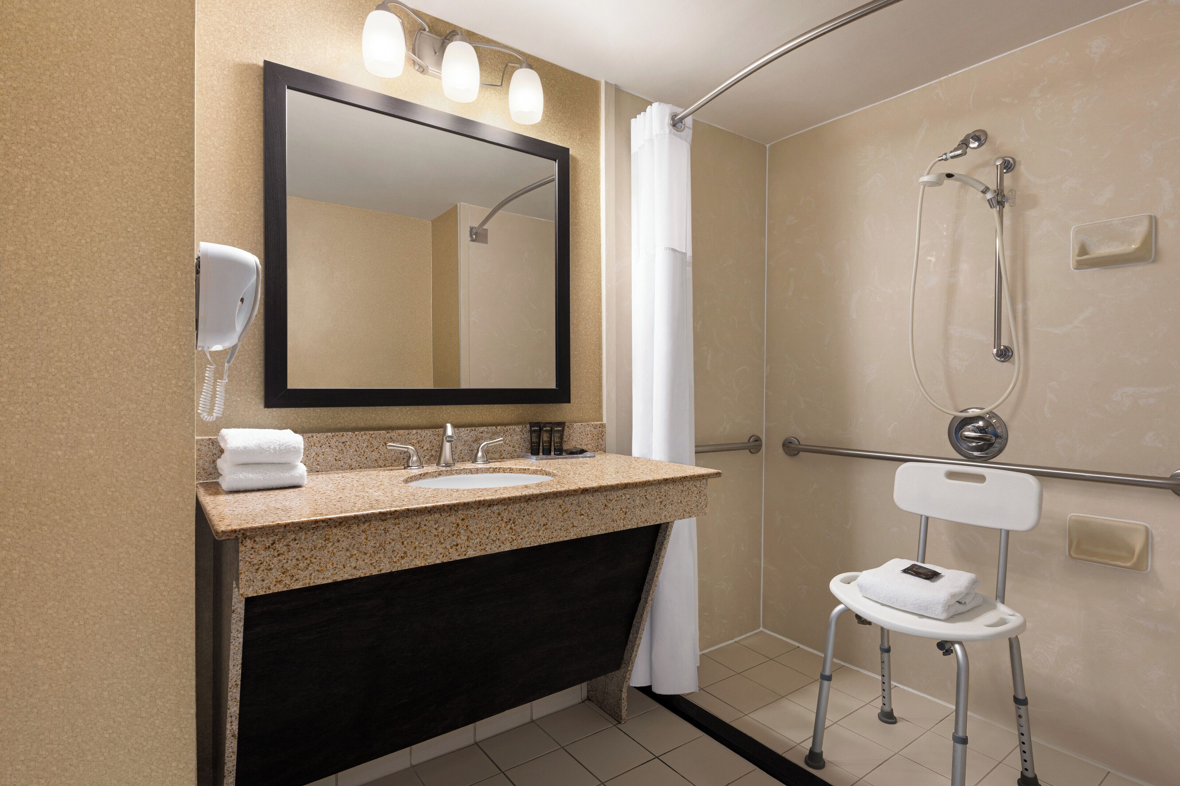 A bathroom with a sink, mirror, towel rack, and a shower with a handheld showerhead.