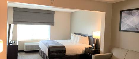 A hotel room with a bed, bedside table, lamp, and a sofa.