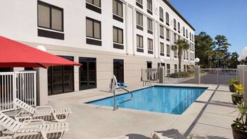 A hotel with a swimming pool, outdoor seating, and a white building facade.