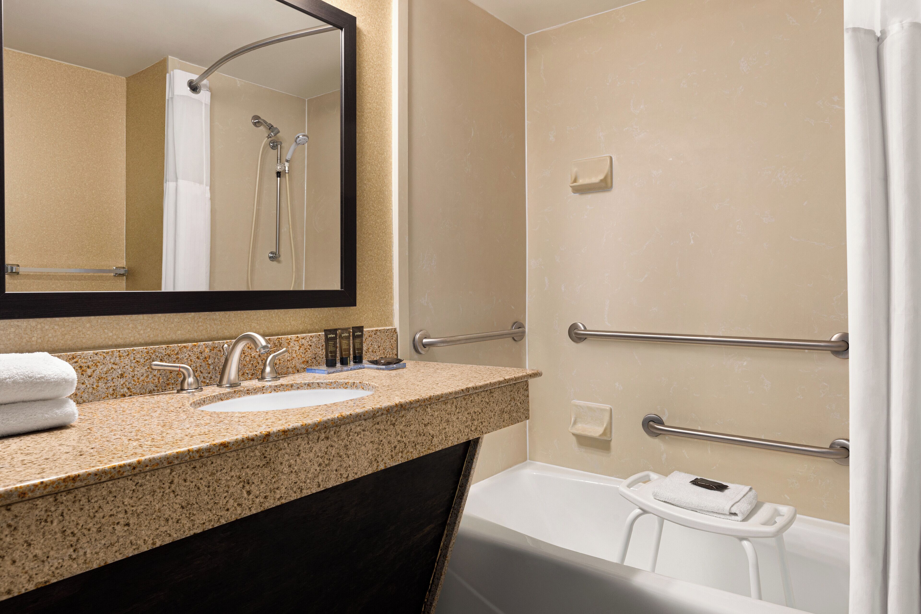 A bathroom with a sink, mirror, shower, and grab bars.