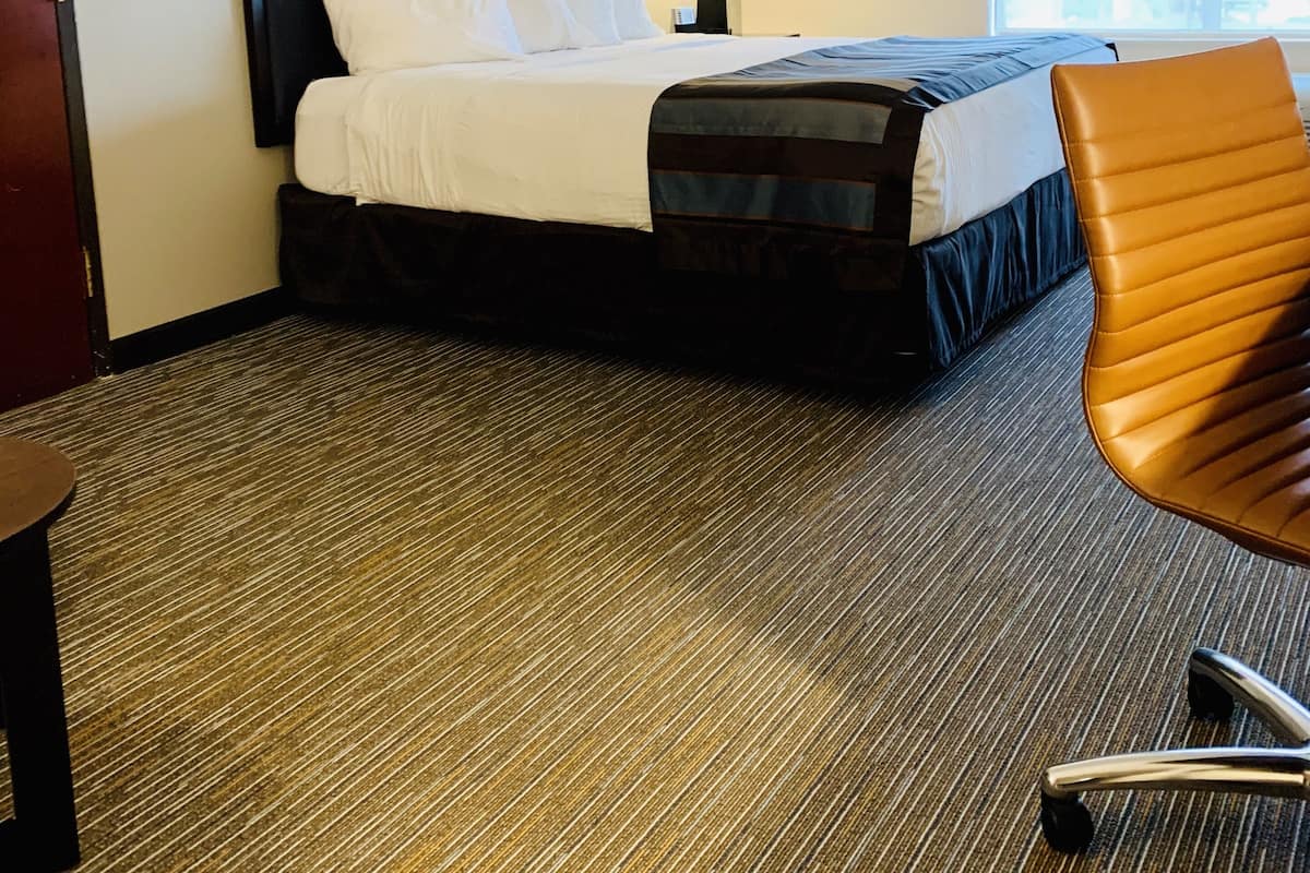 A hotel room with a bed, a chair, a lamp, and a window.