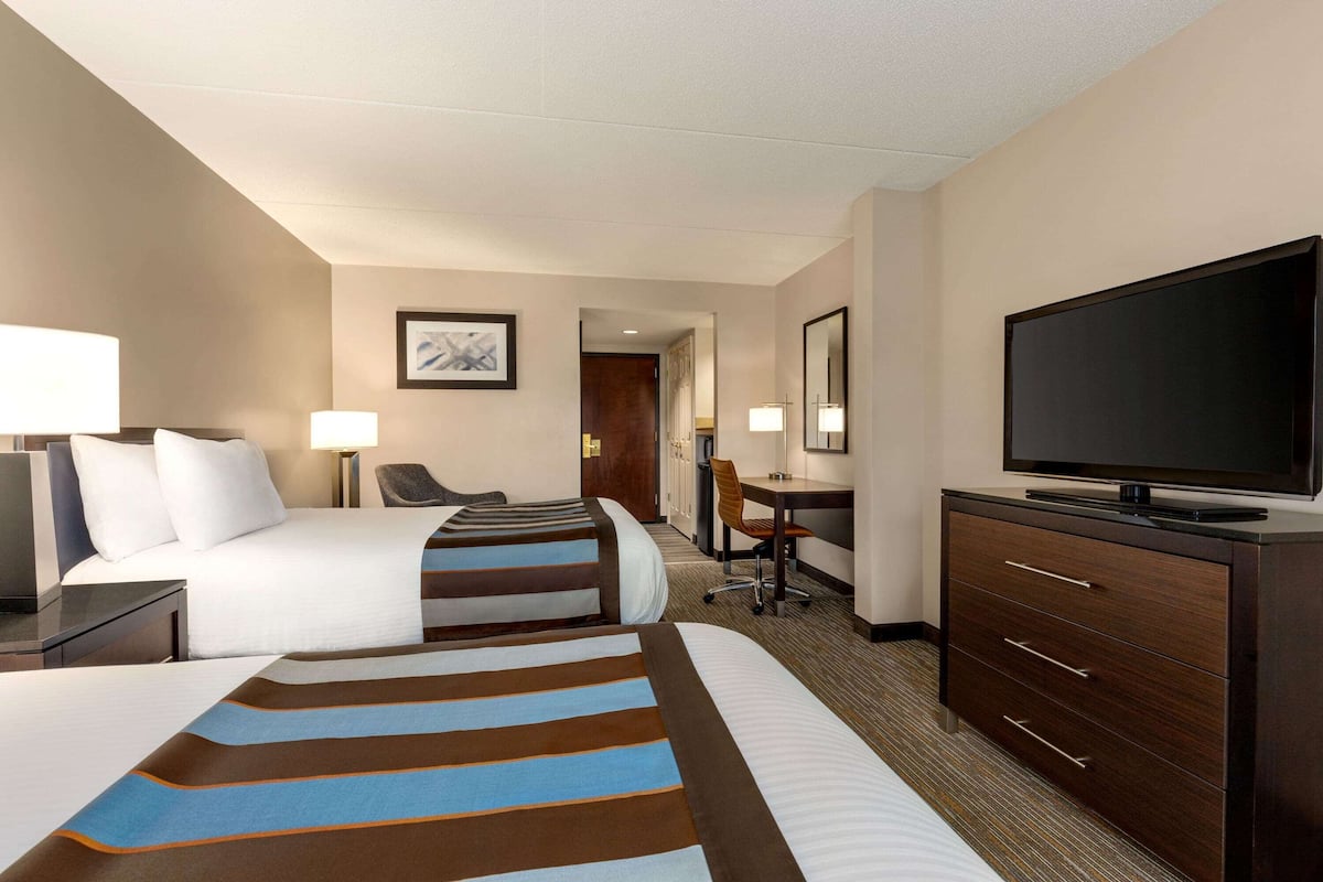 A hotel room with two beds, a desk, a chair, a television, and a dresser.
