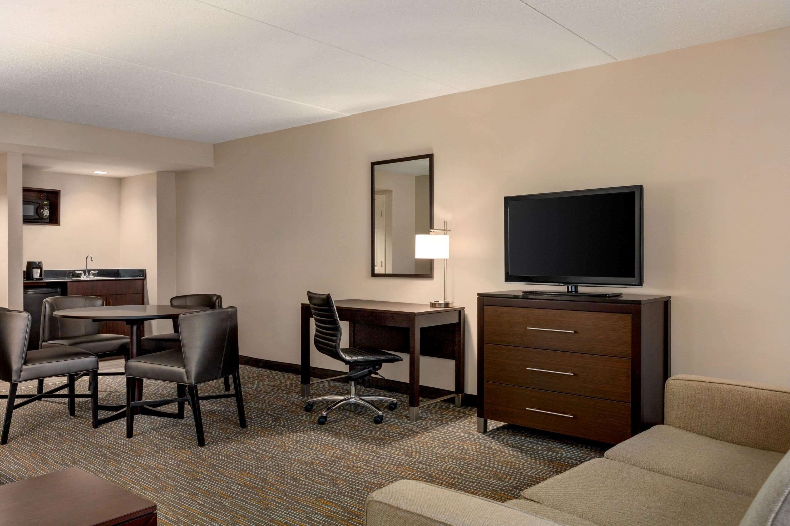 A hotel room with a dining area, a TV, a desk, and a sofa.