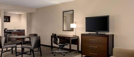 A hotel room with a dining area, a TV, a desk, and a sofa.