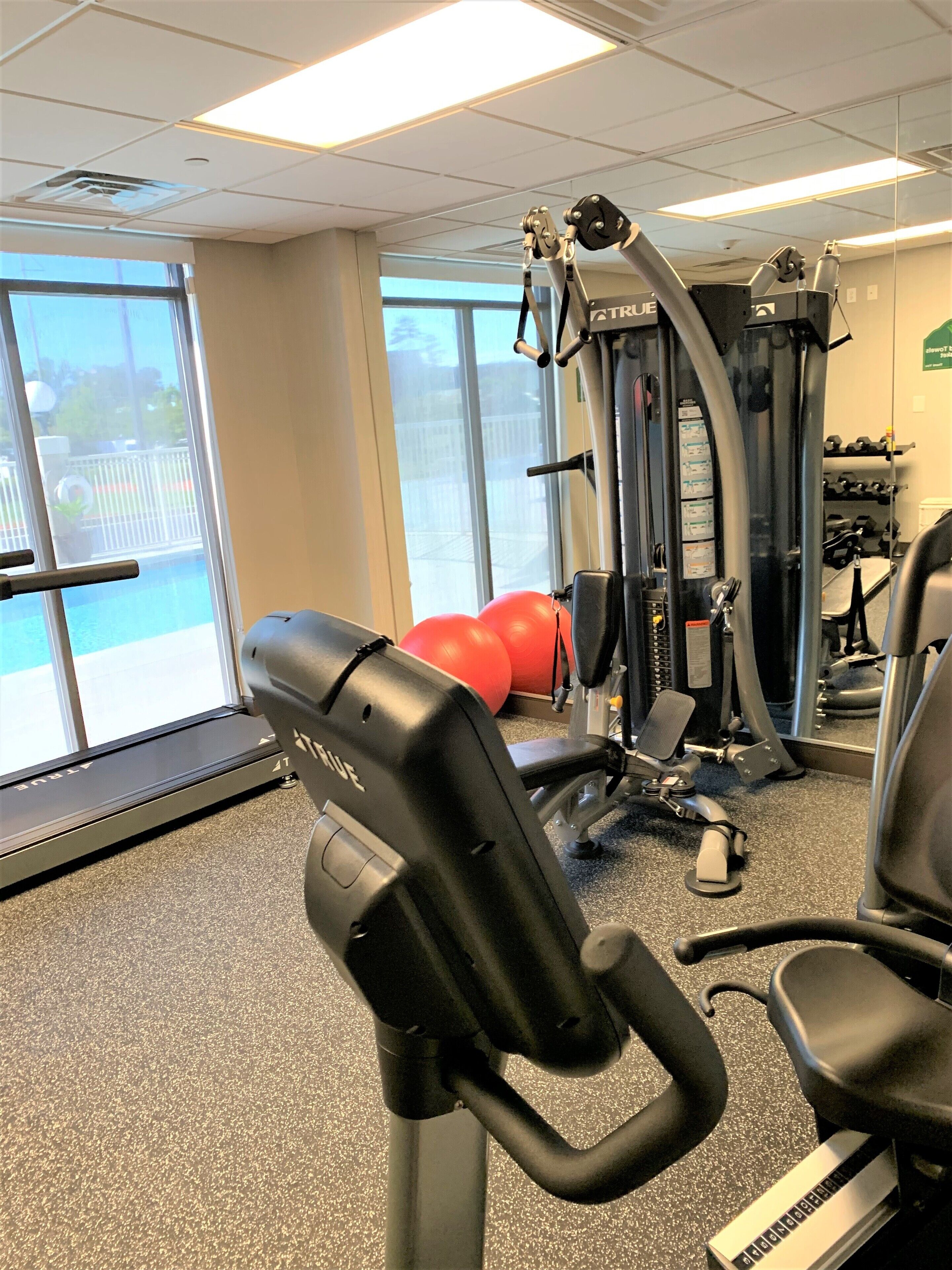 A gym with exercise equipment, a treadmill, and large windows with a view of a pool and outdoor area.