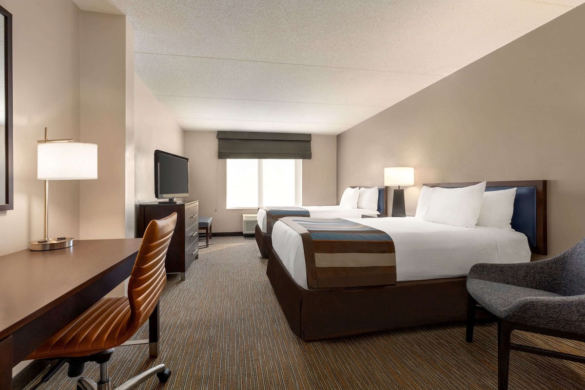 A hotel room with a bed, two bedside tables, a desk with a chair, a TV, and a window with a view.