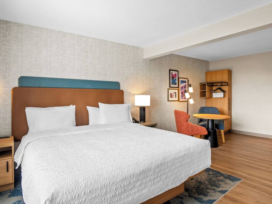 A hotel room with a large bed, bedside tables, a desk, a chair, and a wall-mounted coat rack.