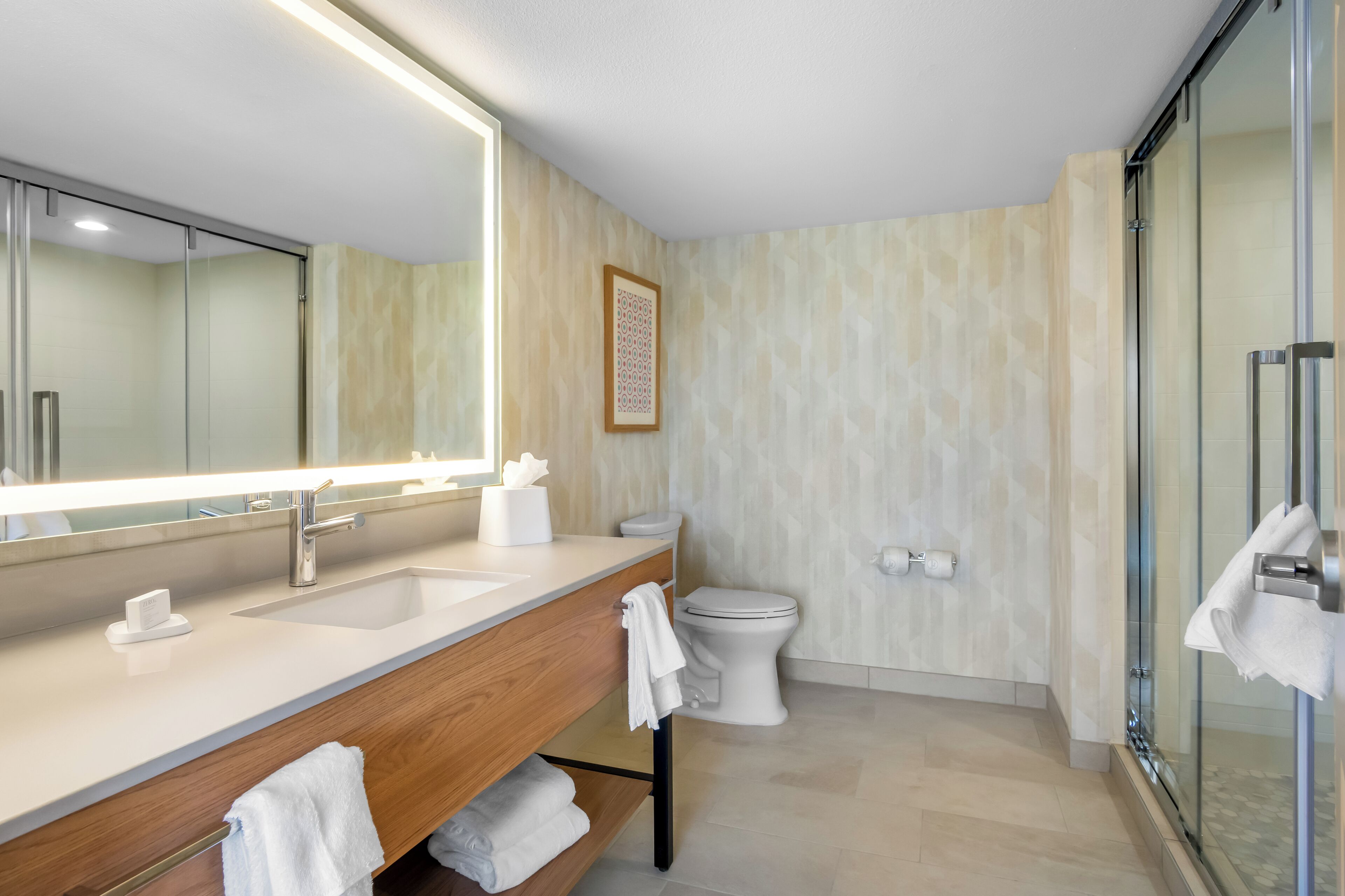 A modern bathroom with a large mirror, two sinks, a toilet, and a glass shower enclosure.
