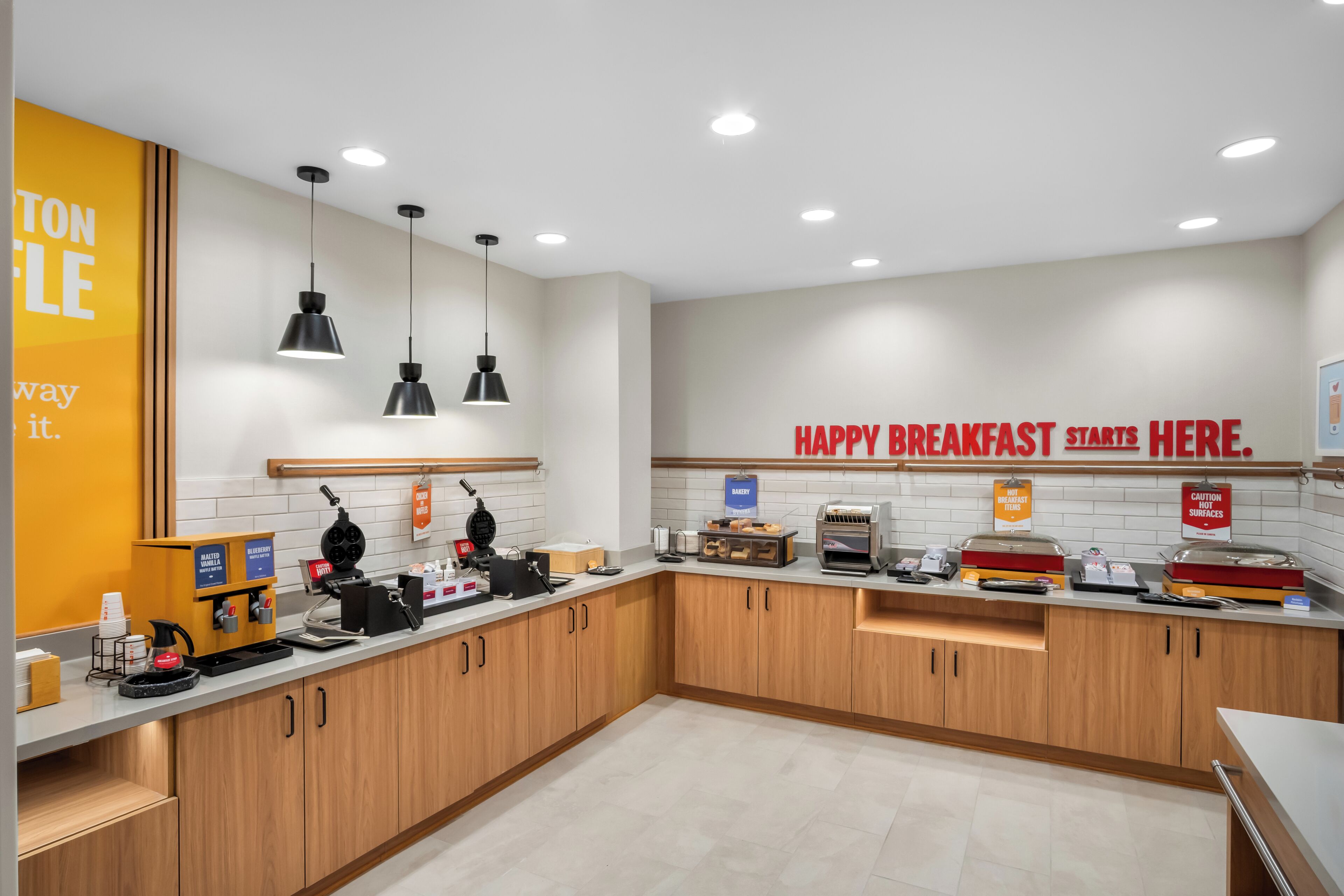 A modern kitchen with wooden cabinets, a coffee machine, and a breakfast sign.