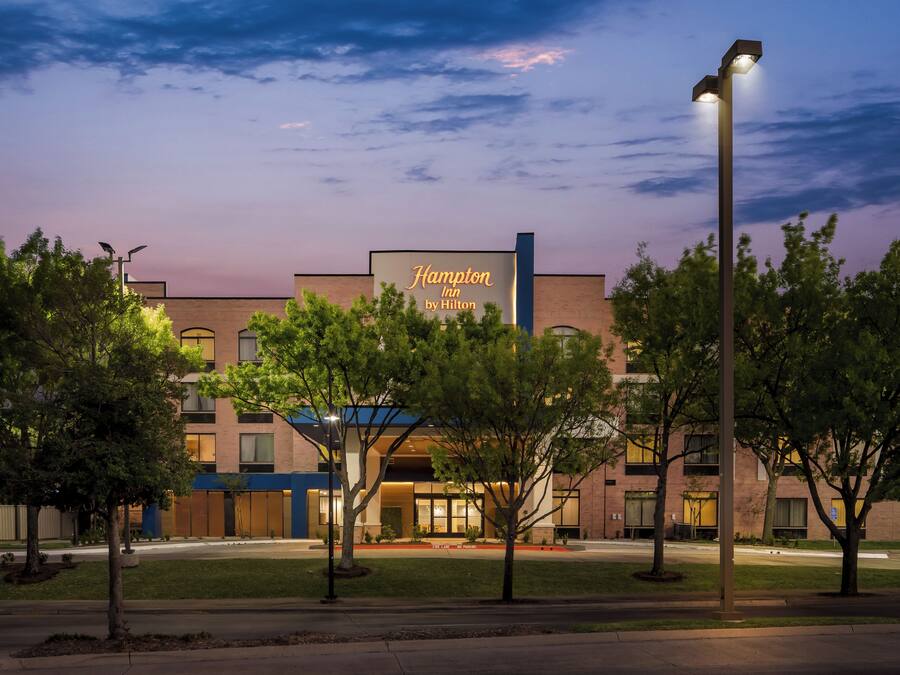 Een Hampton Inn by Hilton hotel met een moderne gevel, grote ramen en een goed verlichte entree.