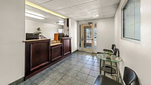 Un área de recepción con un mostrador de madera, una mesa de vidrio con sillas y una puerta que da al exterior.