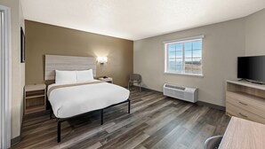 Habitación de hotel con cama, mesita de noche, lámpara, televisor y ventana con persianas.