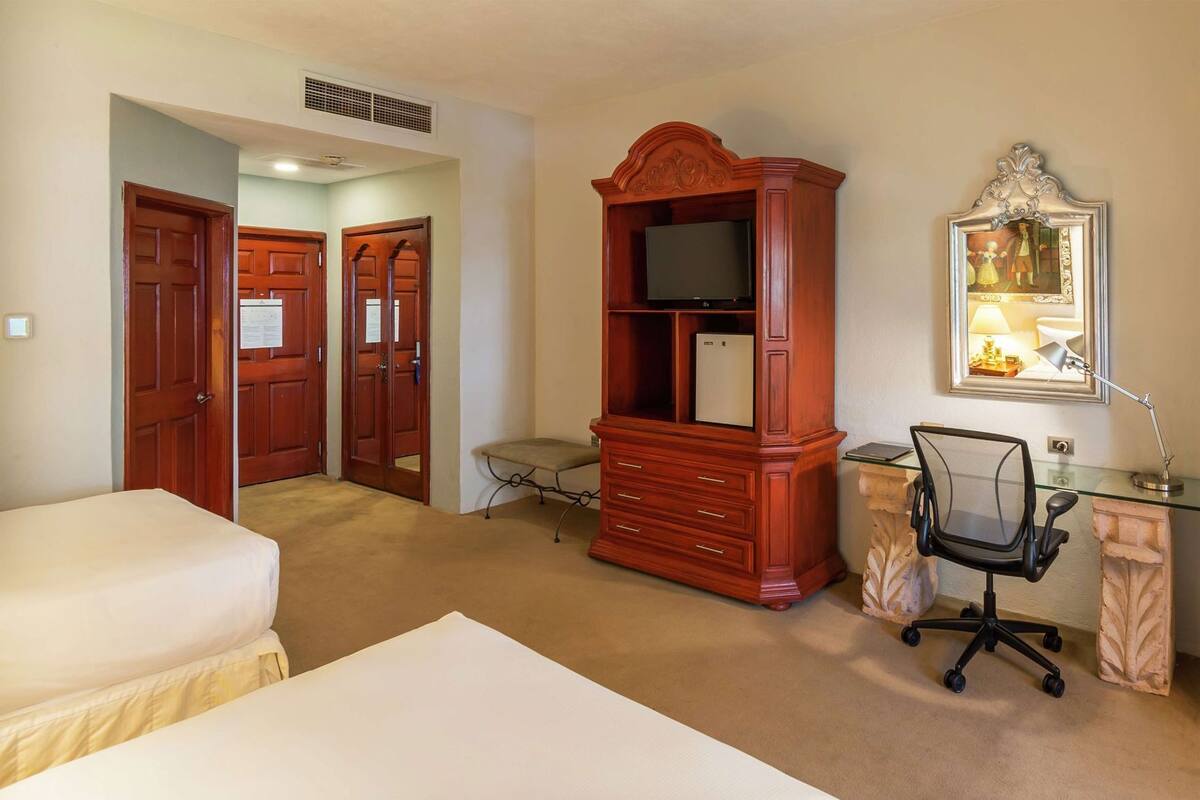 A hotel room with two beds, a wooden entertainment center with a TV, a desk with a chair, and a framed picture on the wall.