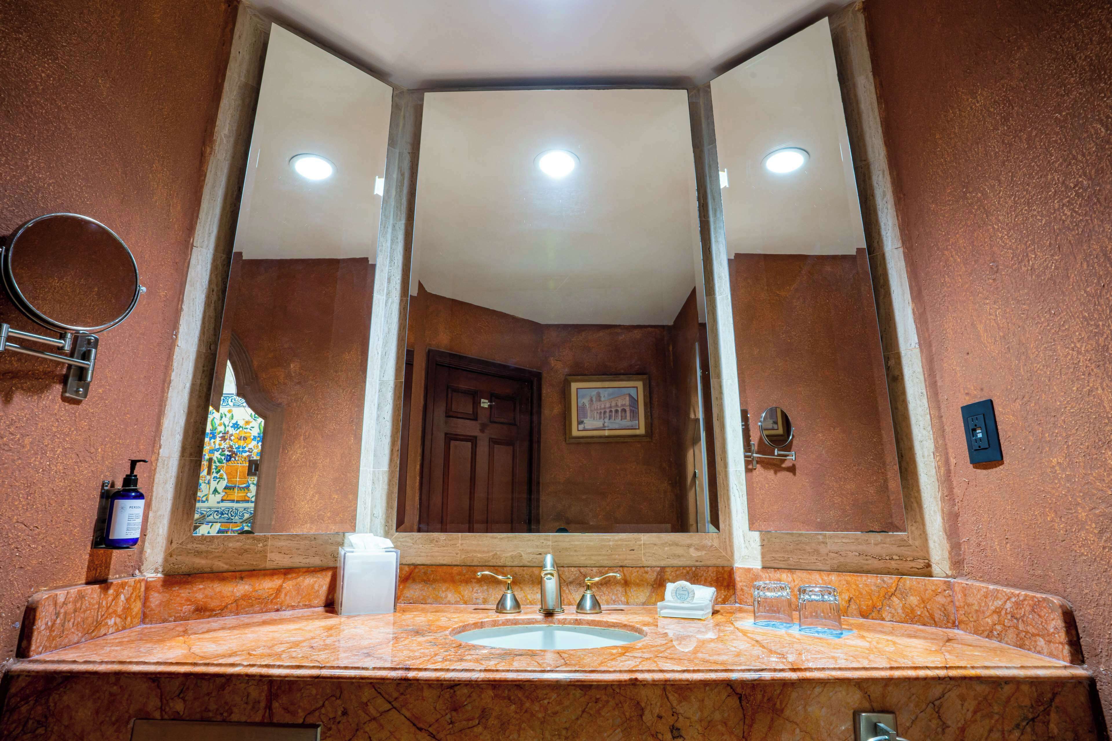 Un baño con un lavamanos de mármol, un espejo grande, una puerta y un pequeño cuadro en la pared.