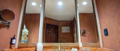 Un baño con un lavamanos de mármol, un espejo grande, una puerta y un pequeño cuadro en la pared.
