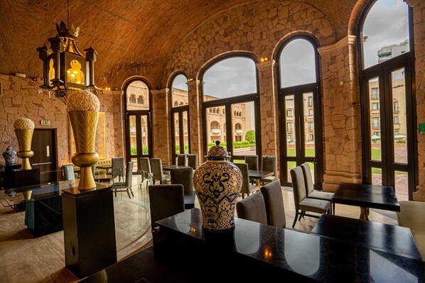 Un restaurante con arcos de piedra, un jarrón grande y vistas a un edificio cercano.
