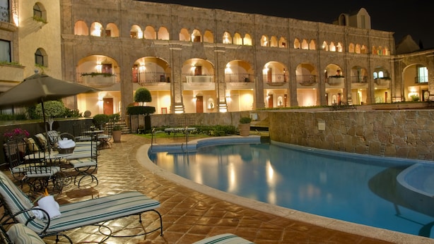 A pool area with lounge chairs and umbrellas, a stone building with multiple balconies, and a clear pool. - Hilton San Luis Potosi (San Luis Potosi)