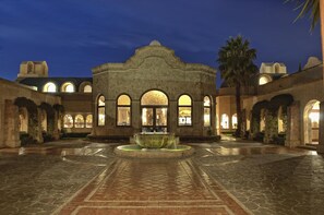 Un patio con una fuente, arcos de piedra y un edificio con ventanas arqueadas.
