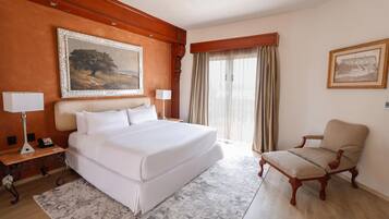 A hotel room with a large bed, a desk with a lamp, a chair, and two framed pictures on the walls.