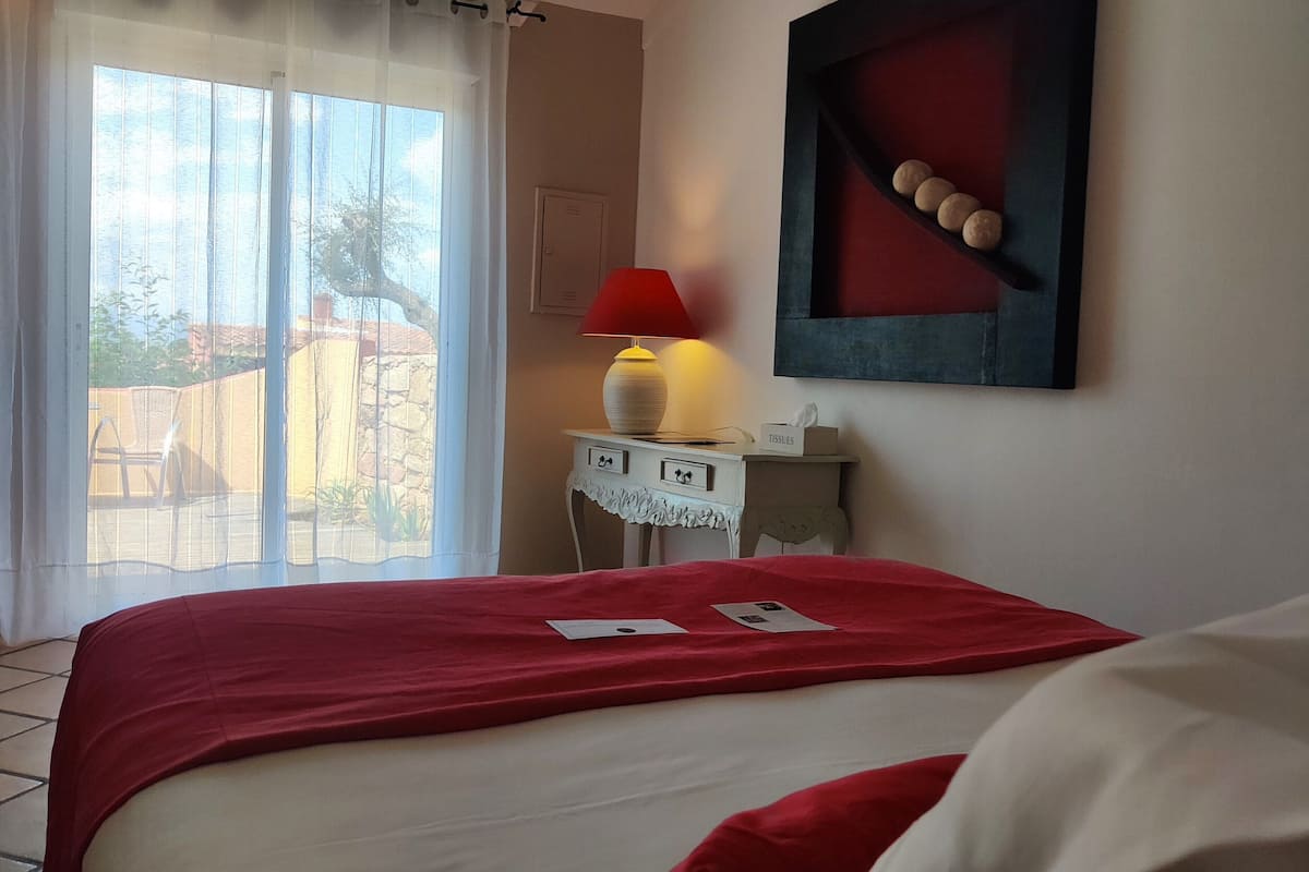 Une chambre d’hôtel avec un lit, une table de chevet avec une lampe, une fenêtre avec des rideaux et un tableau au mur.