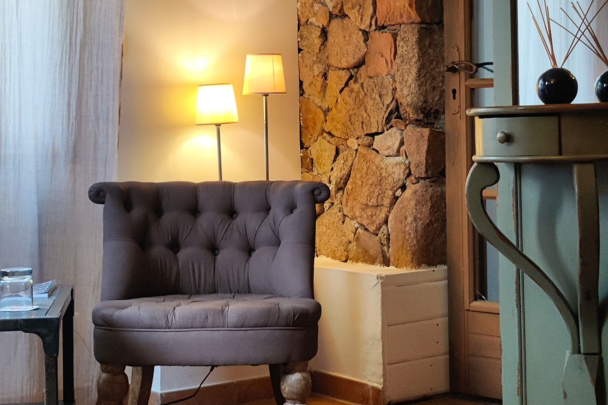 A room with a tufted armchair, a stone wall, and a wooden cabinet with a mirror.
