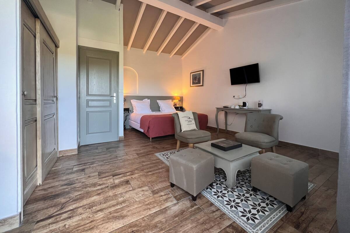 Une pièce comprenant un lit, deux fauteuils, une table basse, un téléviseur et un bureau avec une chaise.