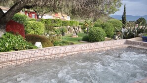 Een jacuzzi omringd door een aangelegde tuin met diverse planten en uitzicht op een heuvel.