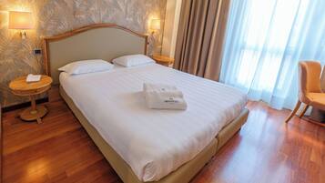 A hotel room with a large bed, a bedside table with a lamp, a chair, and a window with curtains.