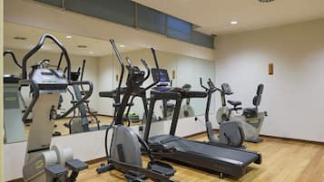 Uma academia com diversos equipamentos de cardio, um espelho grande e piso de madeira.