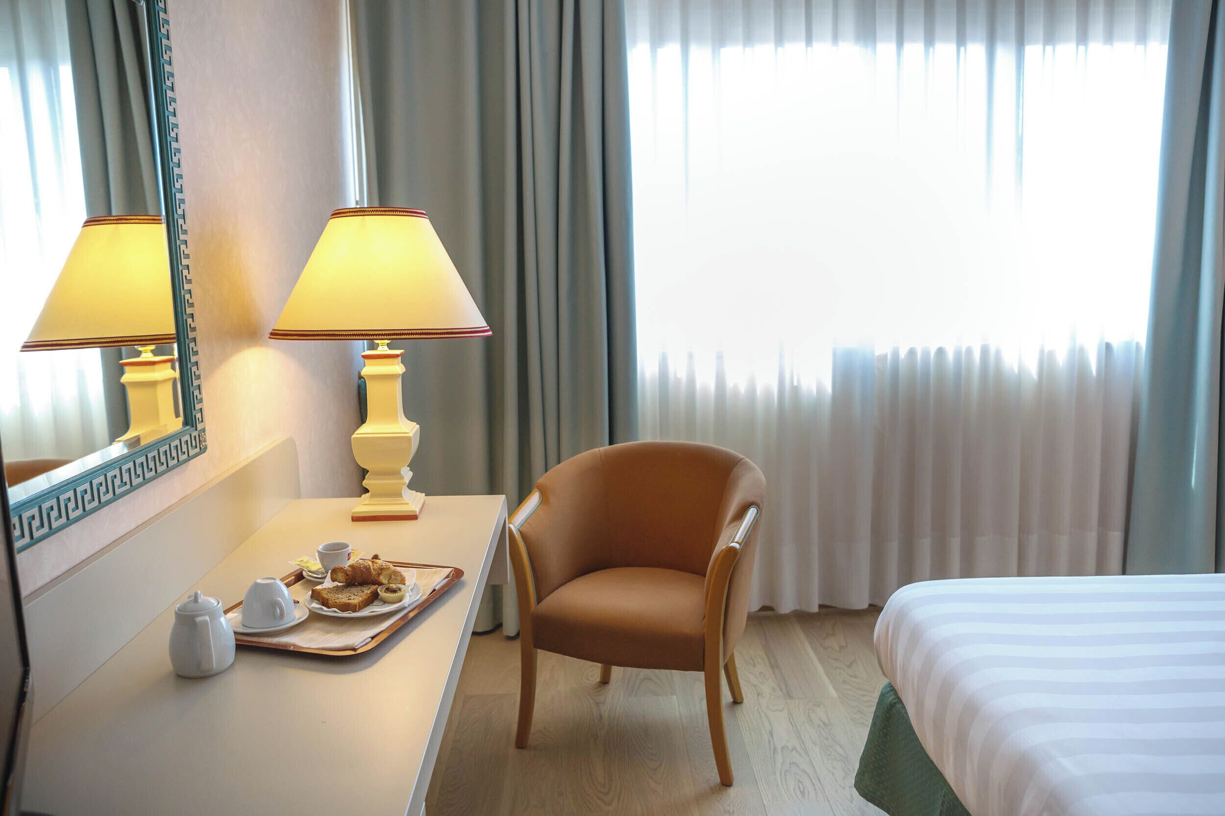 Una habitación de hotel con cama, una silla, una mesa con una bandeja de desayuno y un espejo.