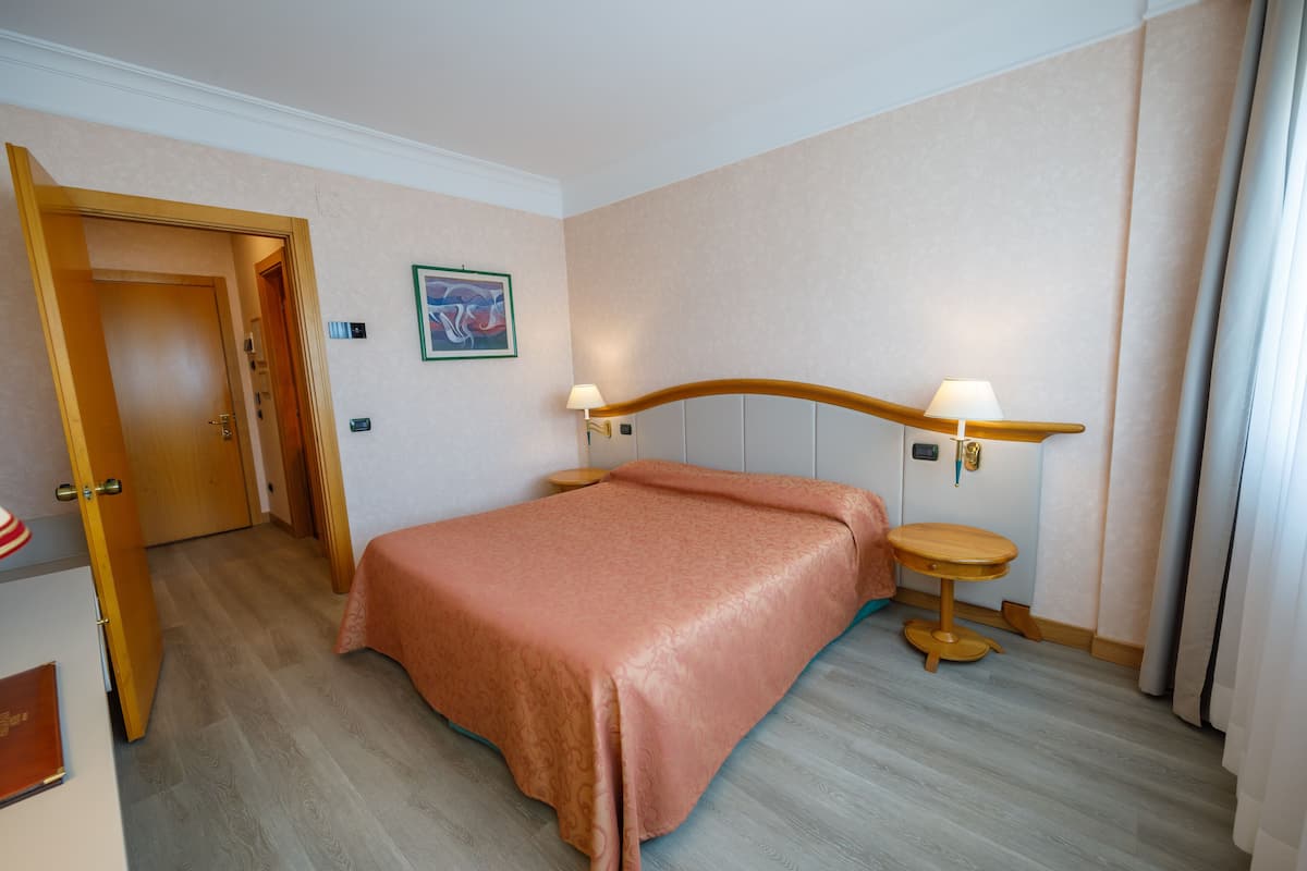 A hotel room with a bed, bedside lamps, a small table, and a door.