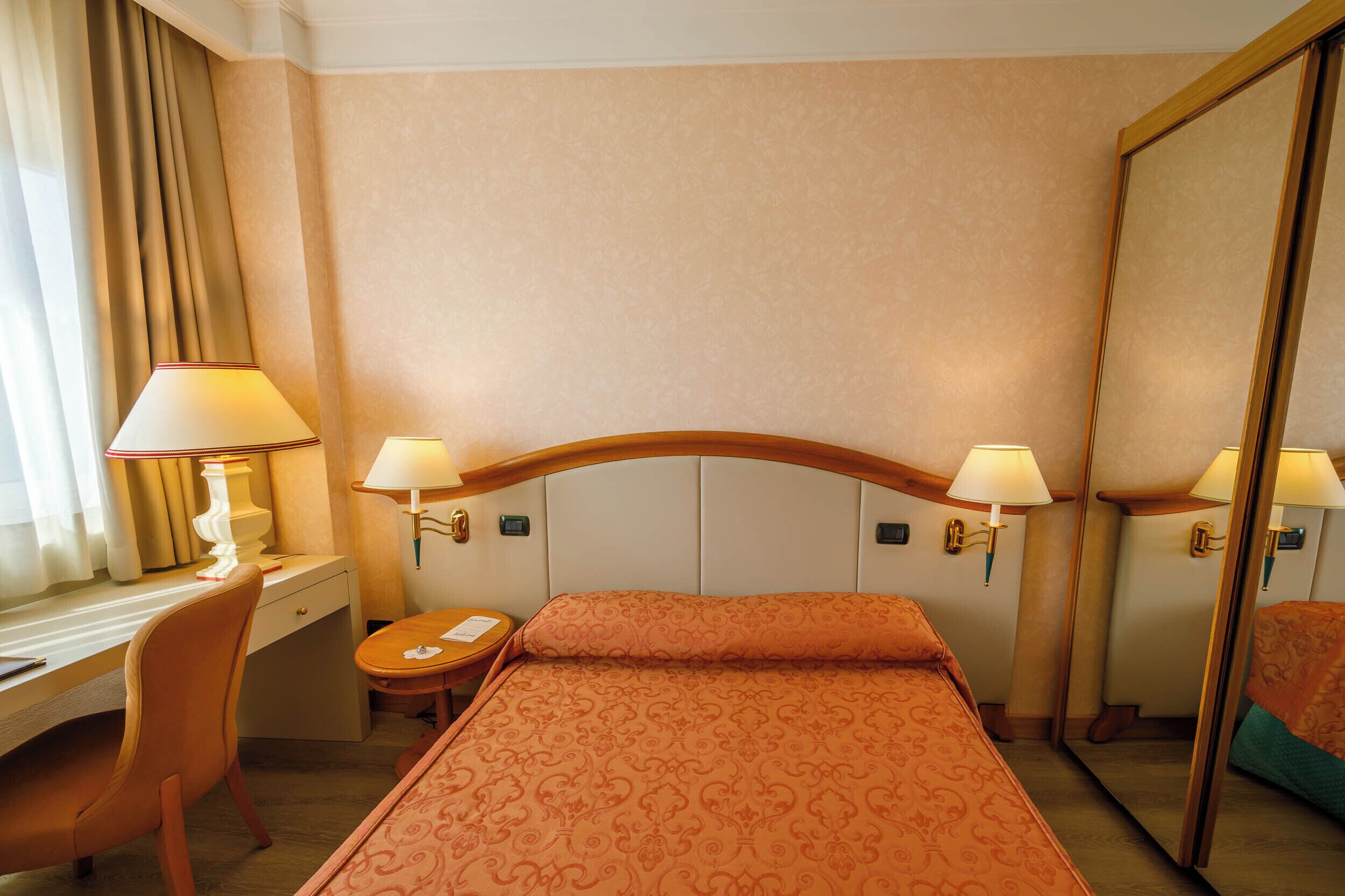 Ein Hotelzimmer mit Bett, Schreibtisch, Stuhl, Lampe, Spiegel und einem kleinen Tisch.