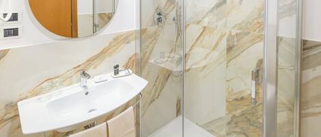 A modern bathroom with a glass-enclosed shower, a marble-tiled floor, a white sink, and a wooden cabinet.