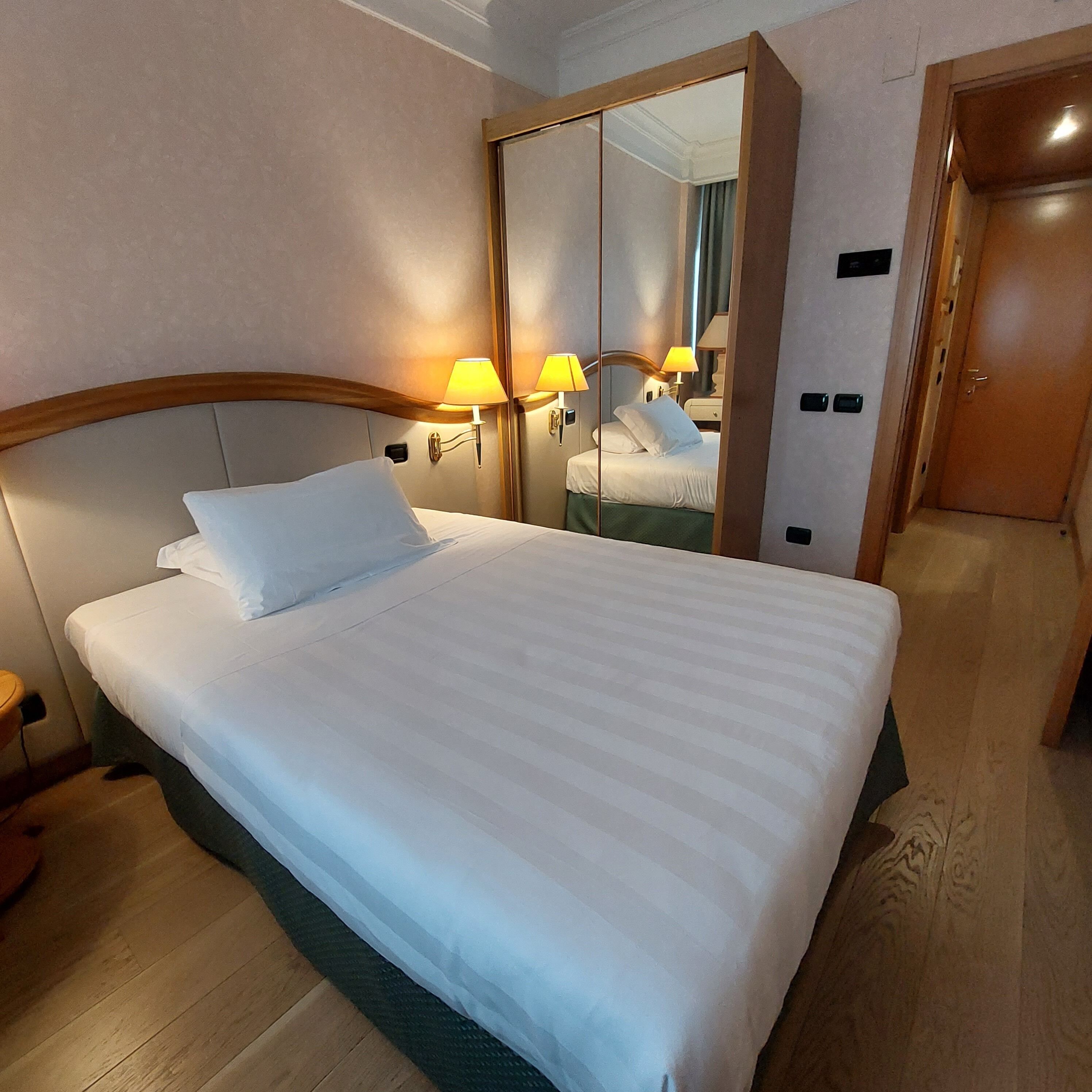 Una habitación de hotel con una cama grande, lámparas de noche, un espejo y una puerta de madera.