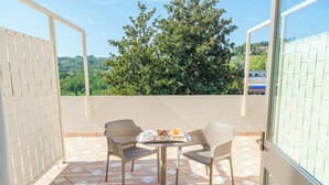 A balcony with two wicker chairs, a small round table with breakfast items, and a view of greenery and buildings. - Hotel Perugia Plaza (Perugia)