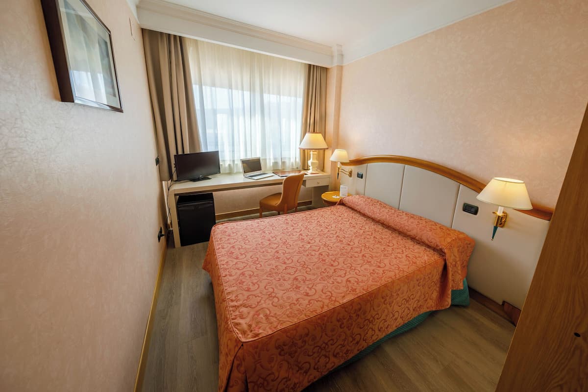 A hotel room with a bed, desk, chair, computer, and two lamps.
