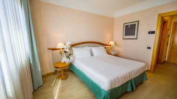 A hotel room with a large bed, two bedside lamps, a small table with a flower, and a door to the right.