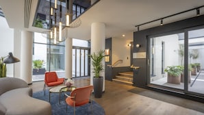 A modern hotel lobby with a curved sofa, a round table, a potted plant, and a staircase leading to an upper level.