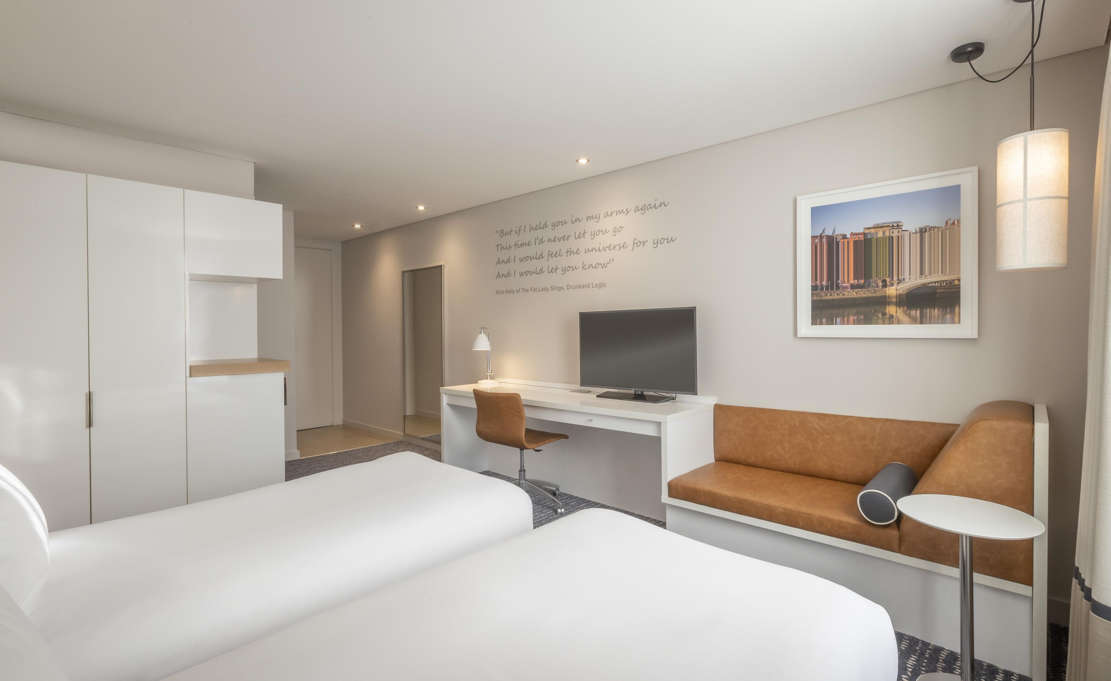 Una habitación de hotel con cama, escritorio con silla, sofá, televisor y lámpara.