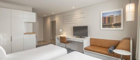 Una habitación de hotel con cama, escritorio con silla, sofá, televisor y lámpara.