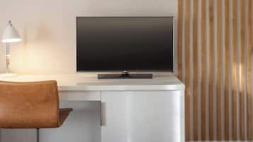 A modern room with a white desk, a flat-screen TV, a brown chair, and a lamp.