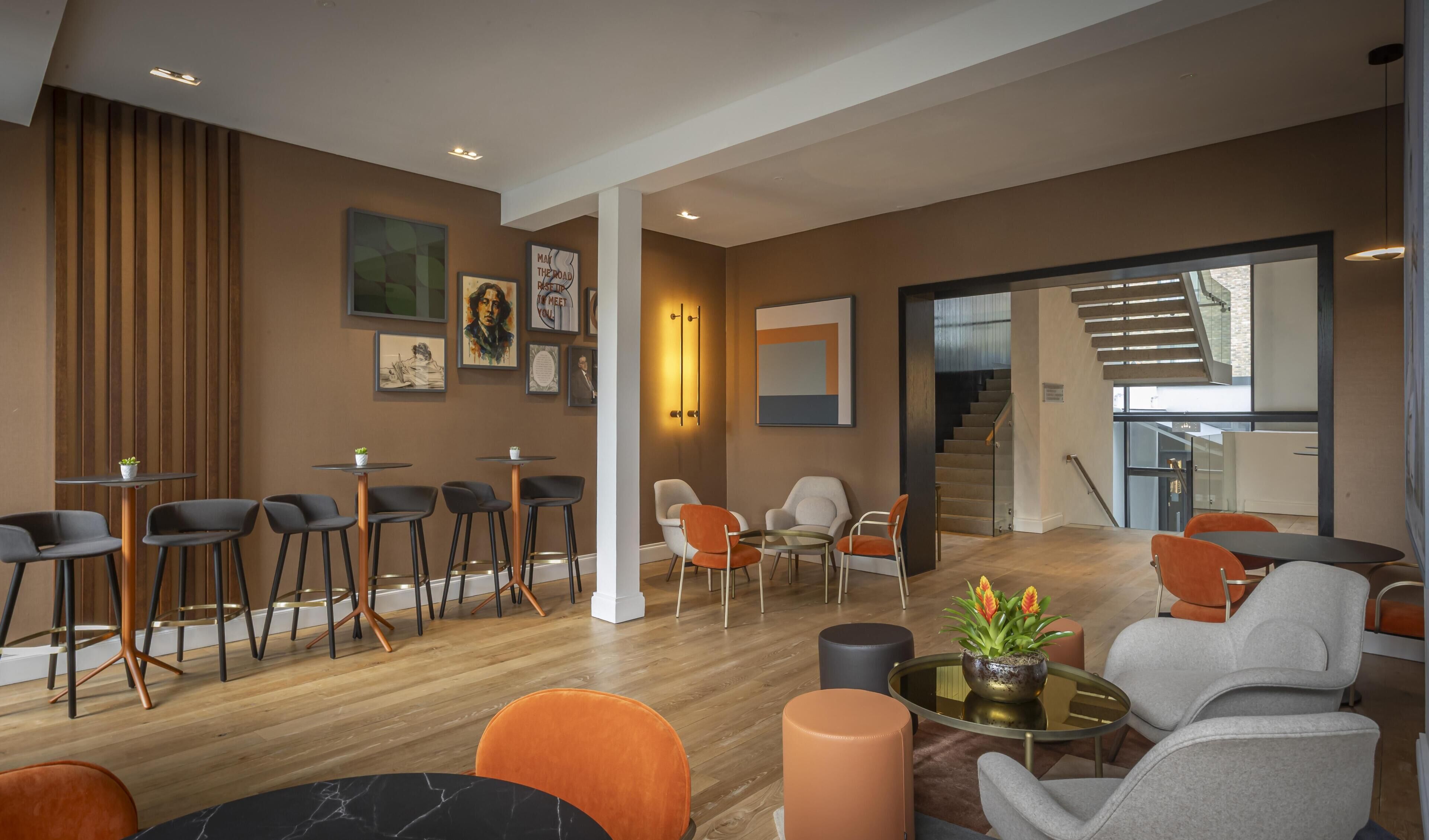 Un área de descanso moderna con diversas opciones de asientos, incluyendo sillones y sofás, una mesa de centro y una escalera que conduce a un nivel superior.