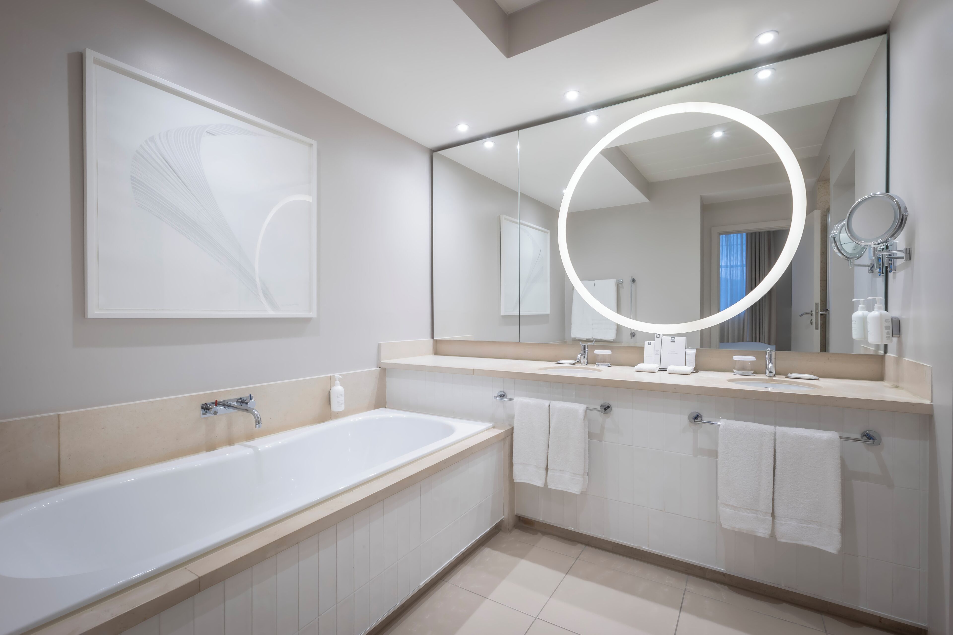 Ein modernes Badezimmer mit einer großen Badewanne, einem Waschtisch mit Spiegel und zwei Handtüchern, die an der Wand hängen.