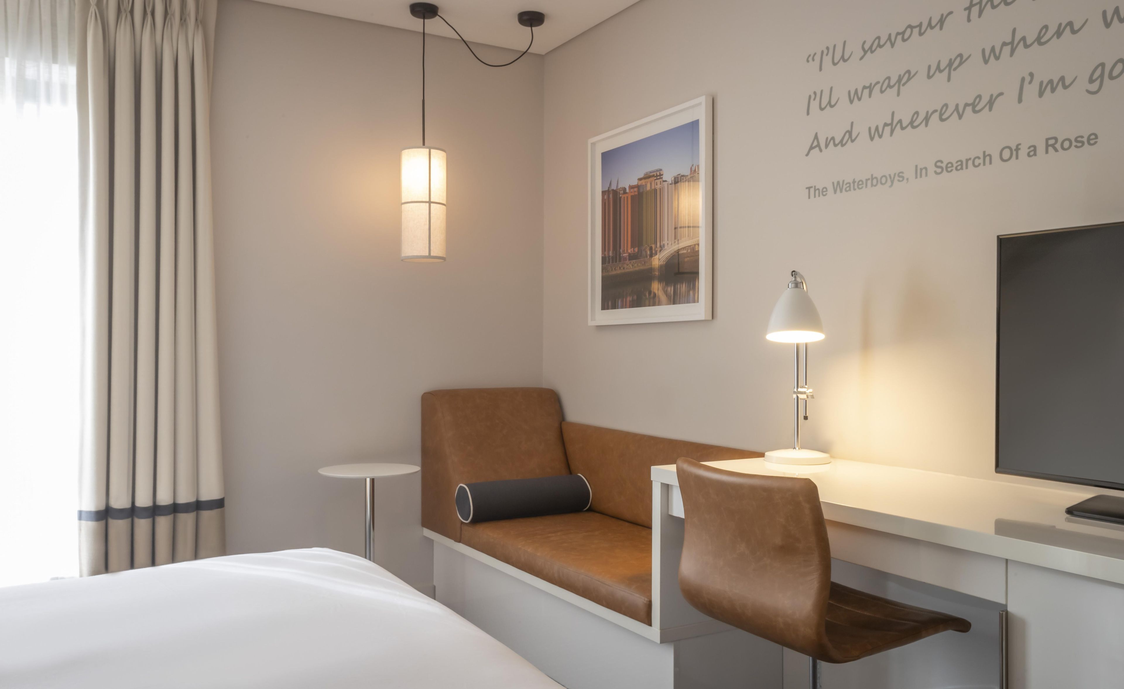 Una camera d'albergo con un letto, un divano, una scrivania con una lampada, una televisione e un quadro appeso al muro.