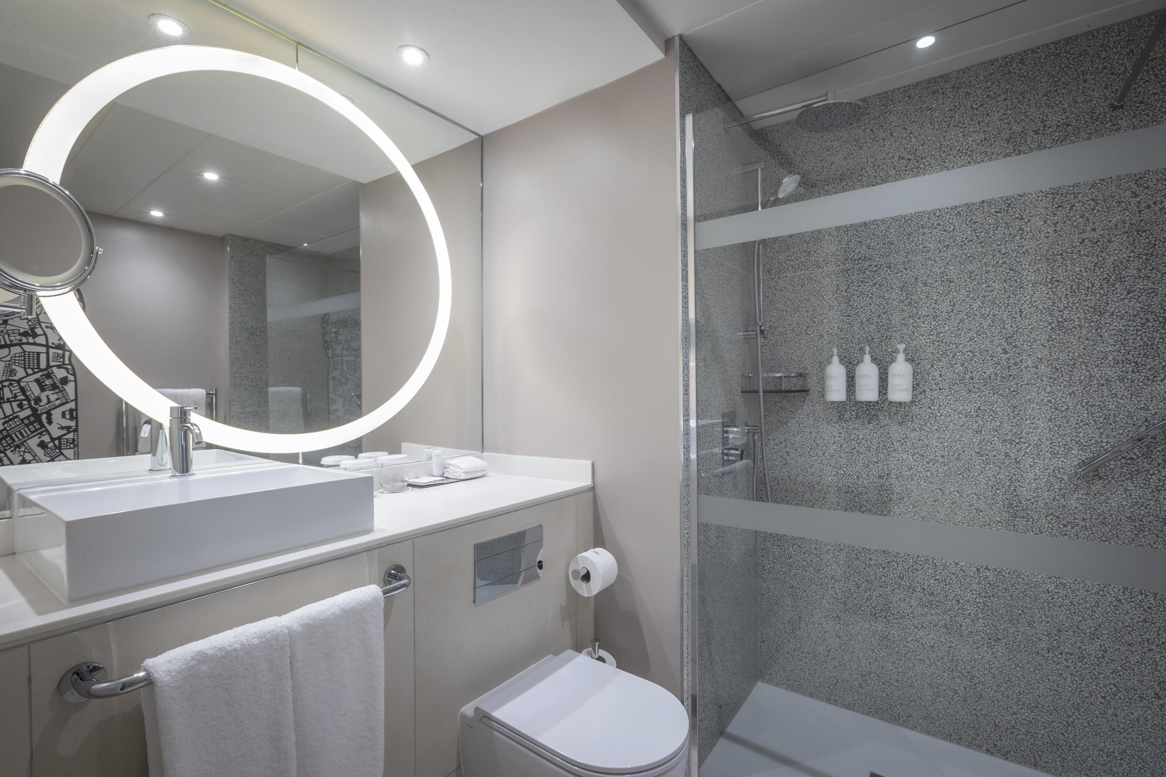 Un baño moderno con un espejo grande, un lavabo, un inodoro y una zona de ducha.
