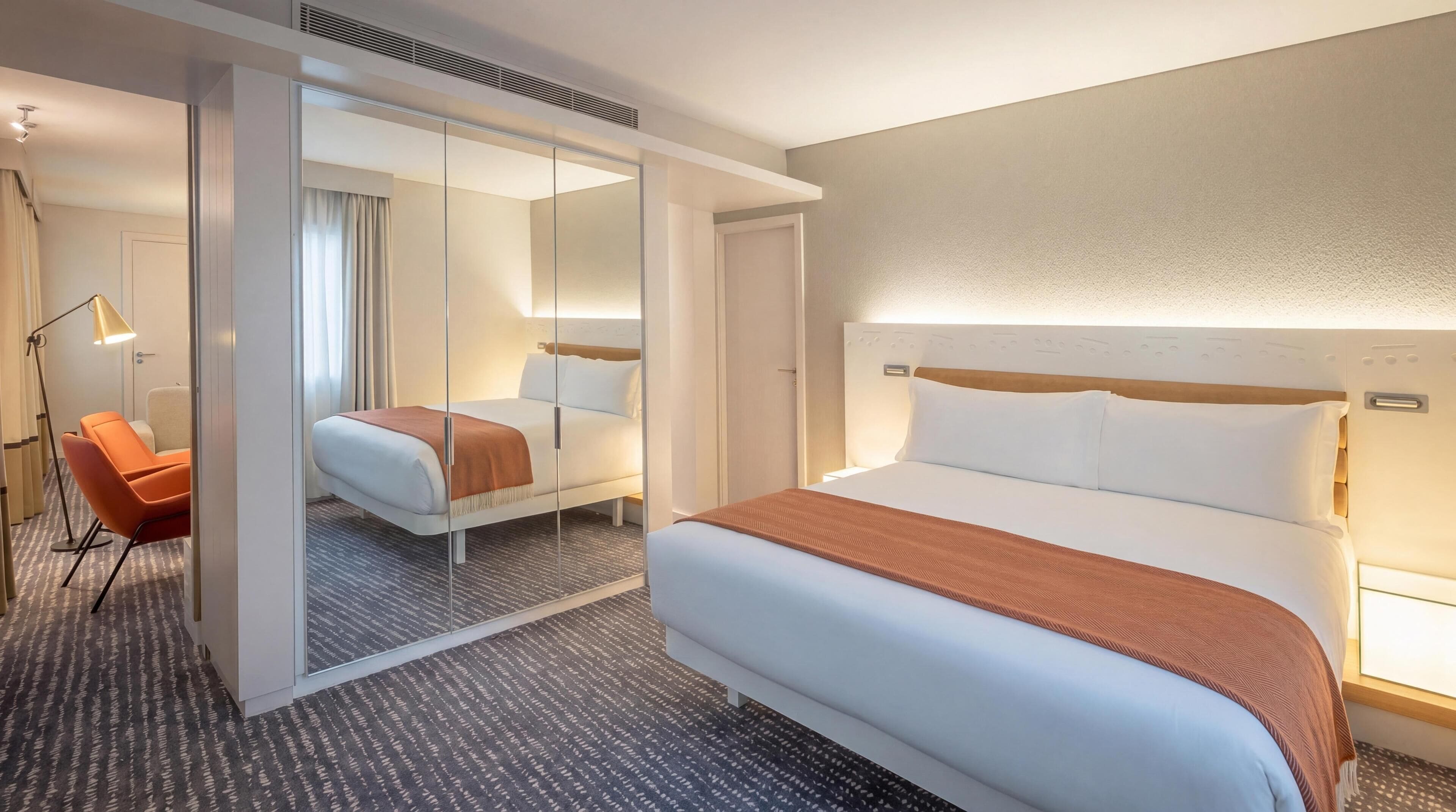 A hotel room with a large bed, a chair, a desk, and a mirror.
